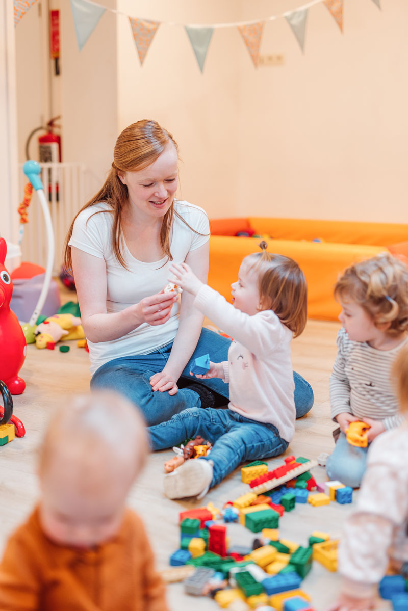 Kinderverzorgster en kinderen samen spelend op de grond.