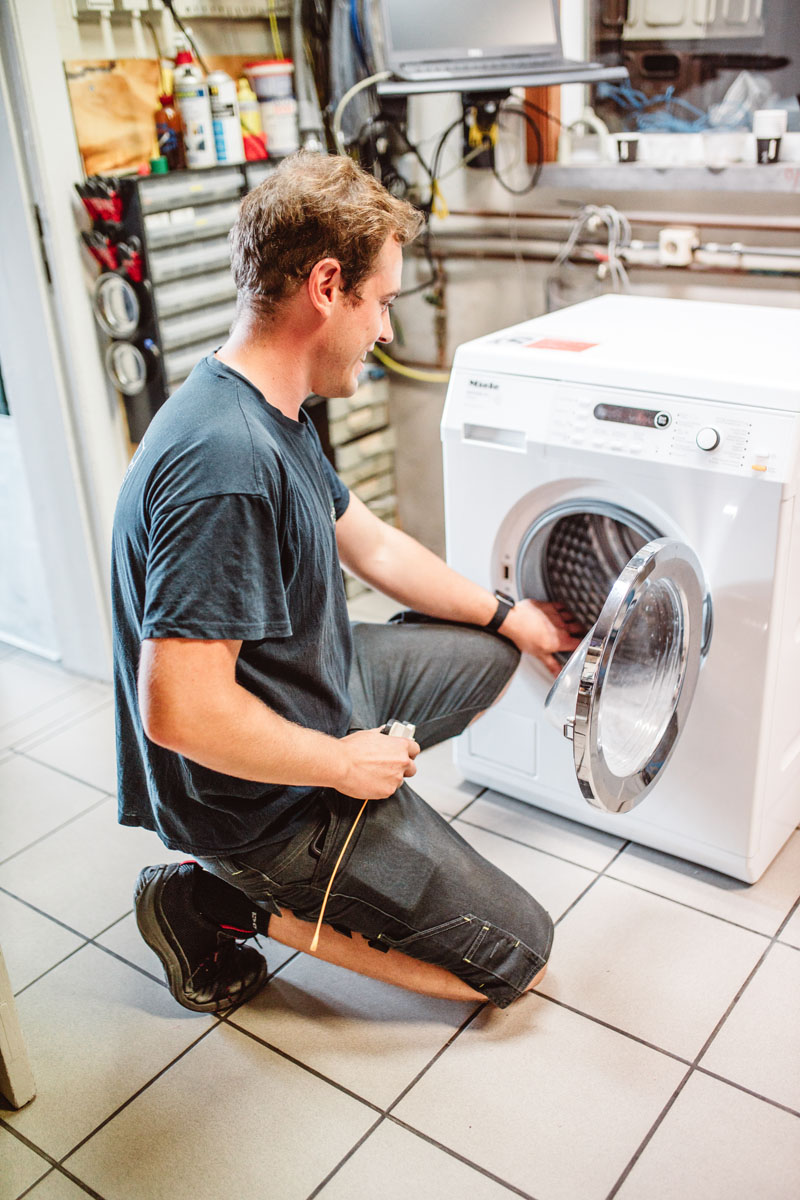 Man die een wasmachine aan het herstellen is.