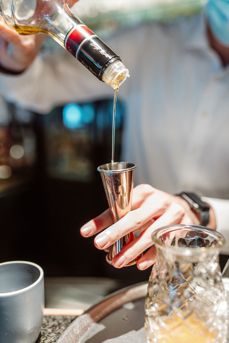 Close up van de barman die een cocktail aan het maken is. Hij giet siroop in een maatbeker.