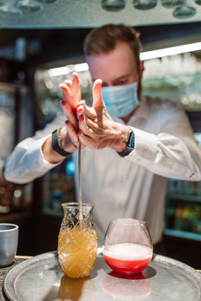 Close up van de barman die een cocktail aan het maken is. Hij mixed de drank met een grote roerstaaf.