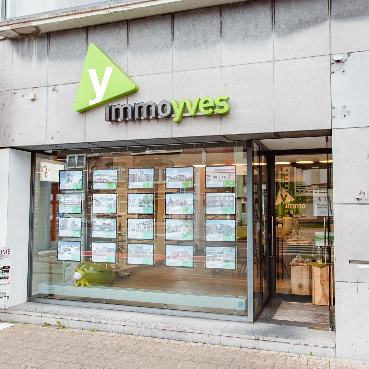 Gevel van Immo Yves met boven het raam zijn logo. In de vitrine alle panden die verkocht of verhuurd worden.