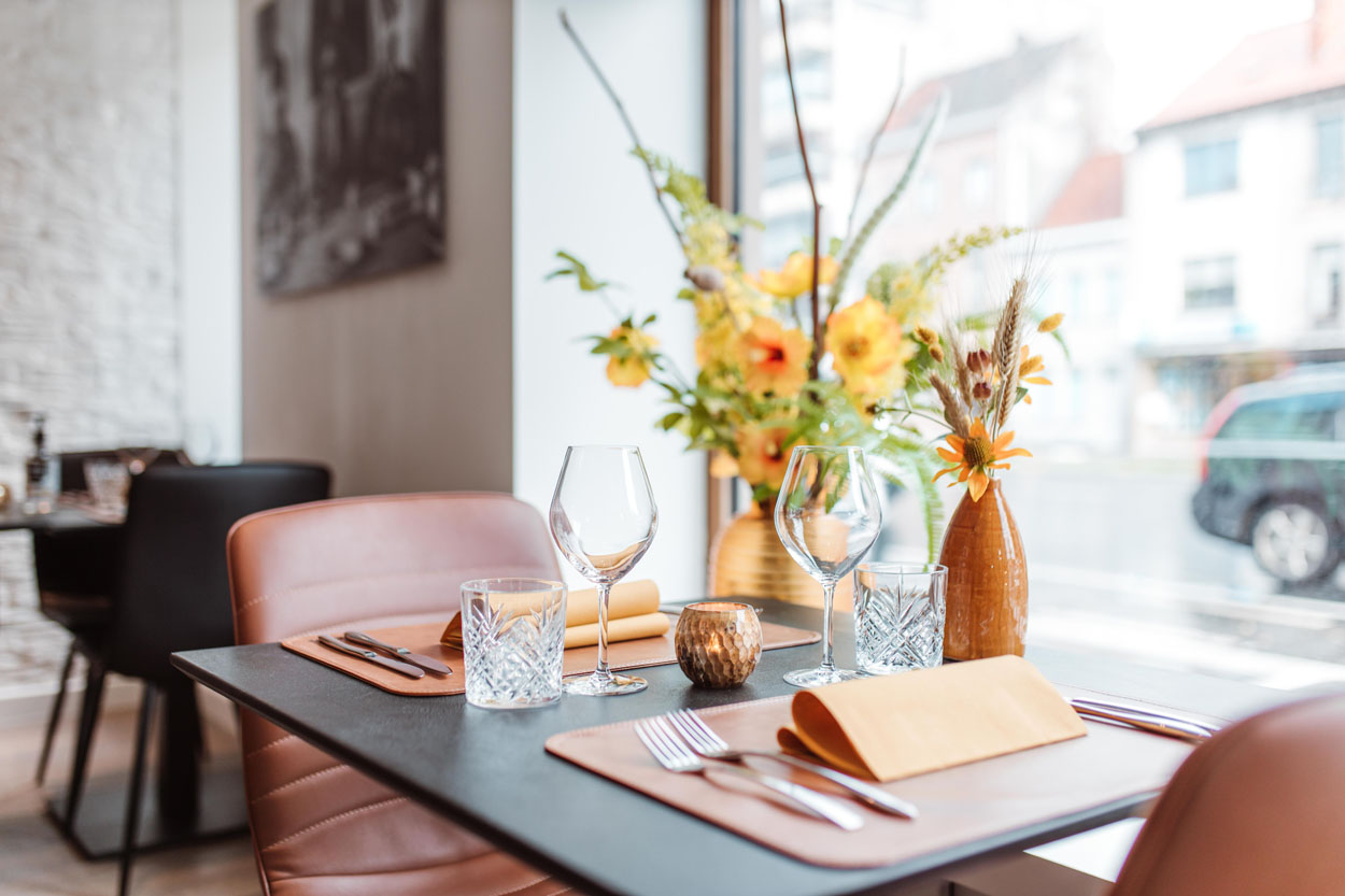 Elegant gedekte tafel met wijnglazen, servietten en een geel boeket op de achtergrond.