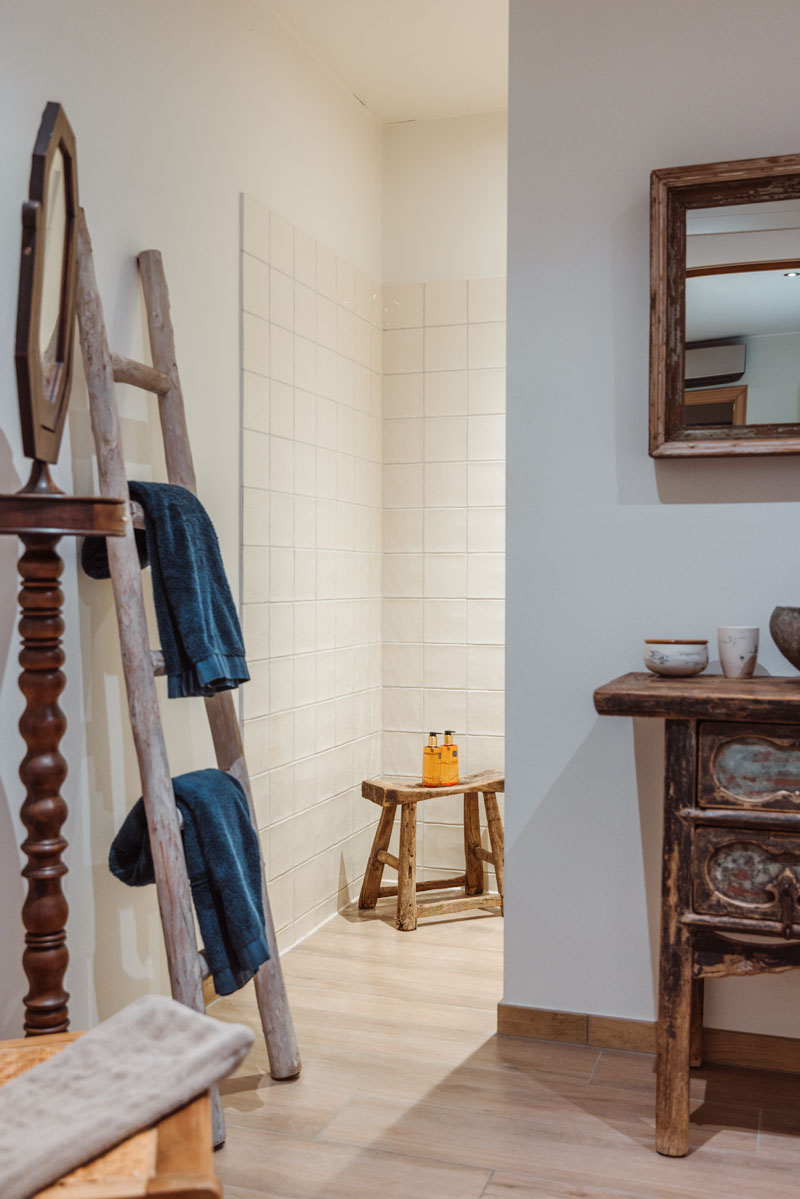 Sfeerbeeld in de badkamer met links een houten deco ladder met daarop blauwe handdoeken.